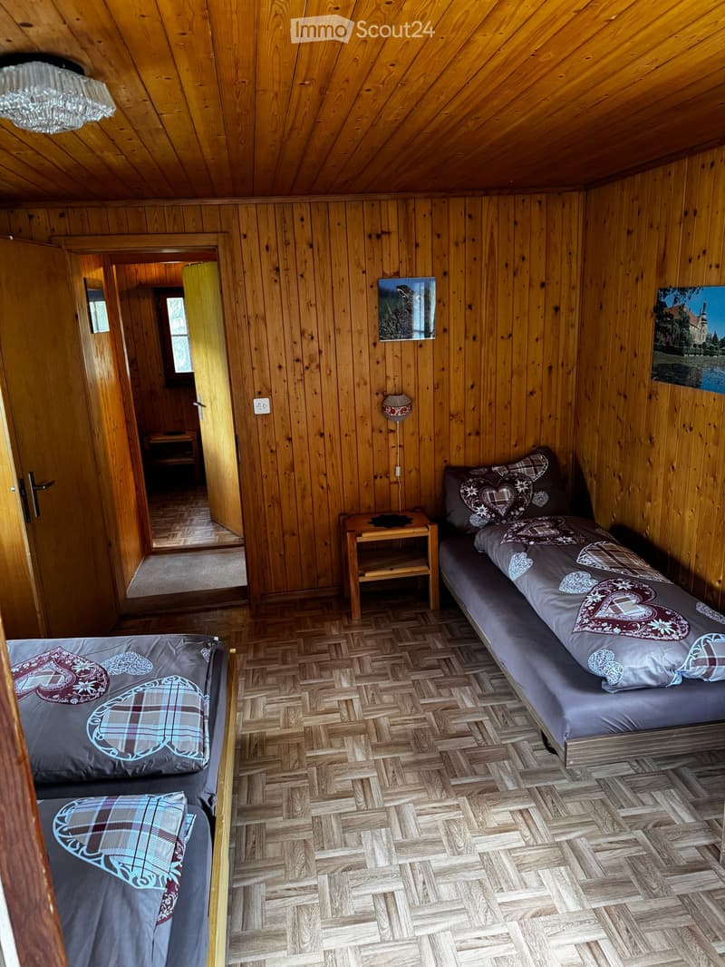 Cozy wooden bedroom with two single beds, nightstand, lamp, and artwork on the walls.