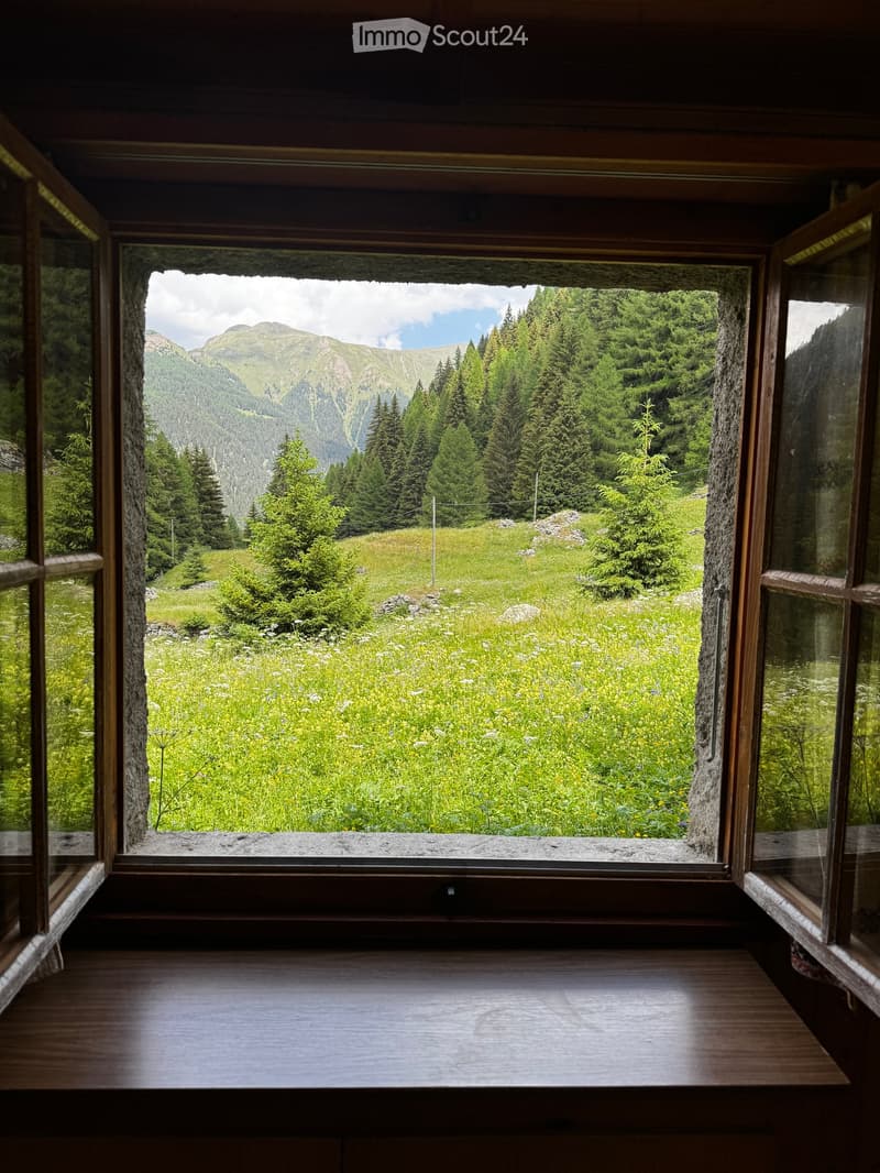 Open wooden balcony with expansive mountain and forest view, stone frame, wooden floor.
