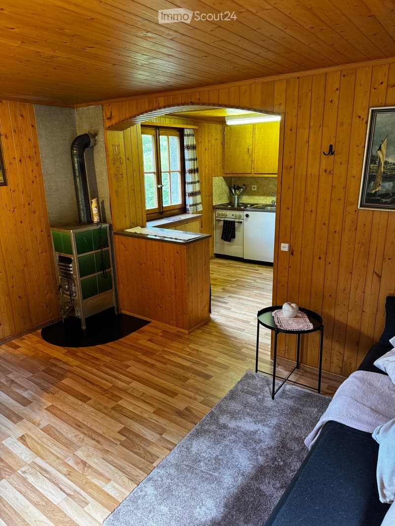 A cozy, wooden-paneled room with a bed, small table, and kitchen area featuring an oven and fridge.