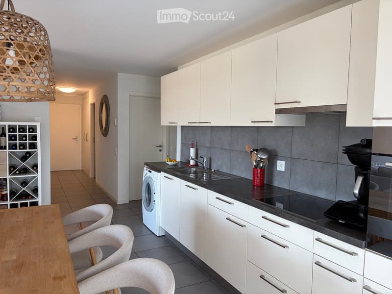 Modern kitchen with white cabinets, black countertops, and stainless steel appliances. Includes a sink, faucet, wine rack, and a small dining area with chairs and a table.
