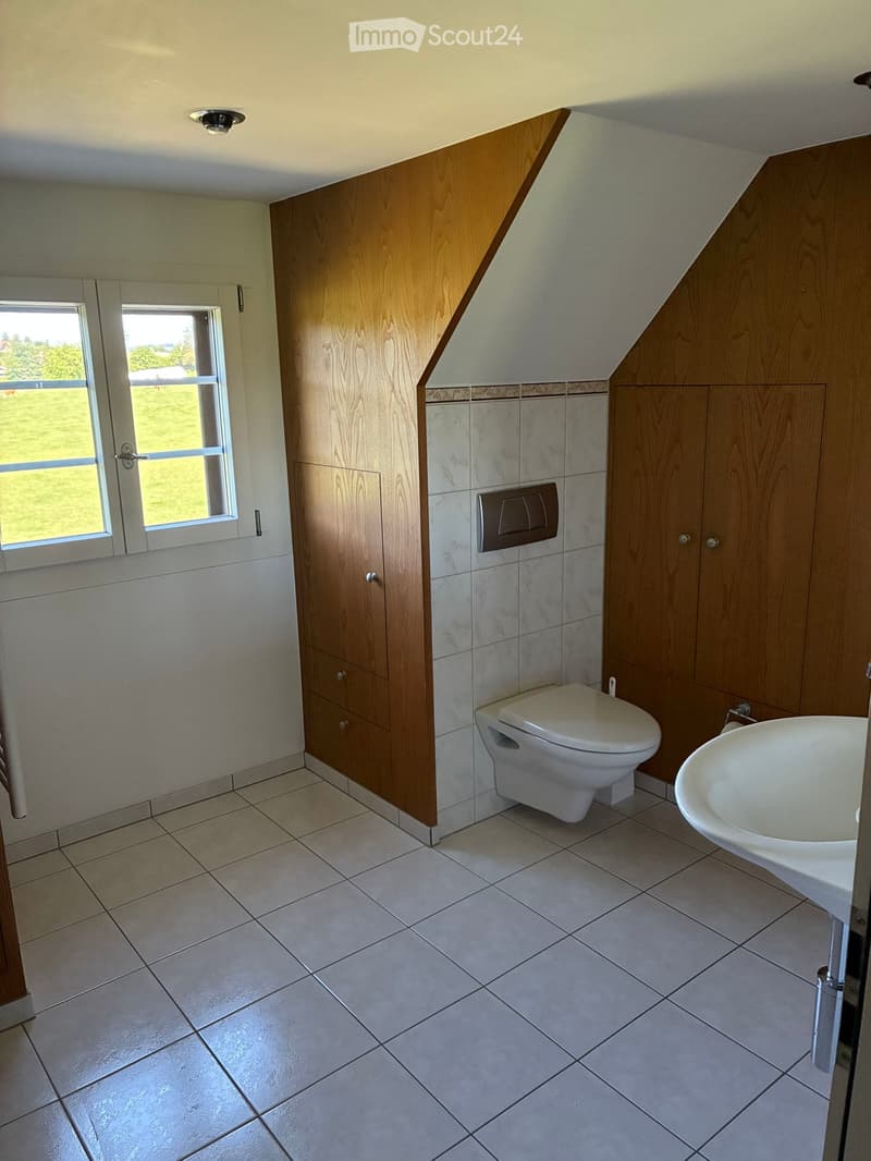 Modern bathroom with white tiled floor, marble wall tiles, wooden cabinets, toilet, and sink.