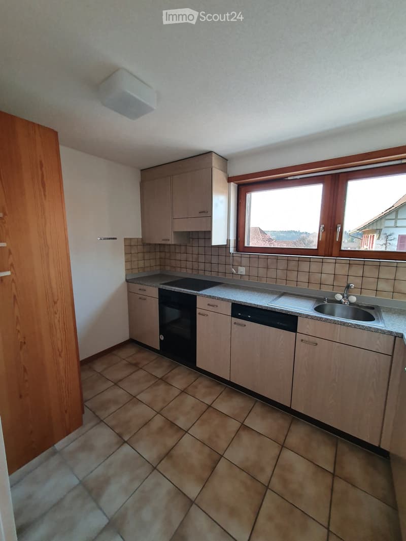 Modern kitchen with light wooden cabinets, granite countertop, sink, oven, and dishwasher. The space features tiled walls and a large window offering a view of the surrounding area.