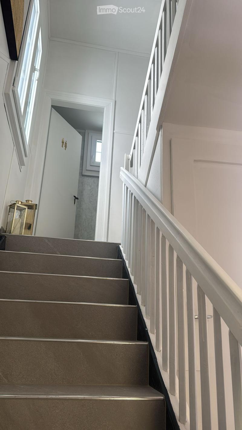 Staircase with gray carpeted steps and white wooden railing, leading to an open doorway with a view of another room.
