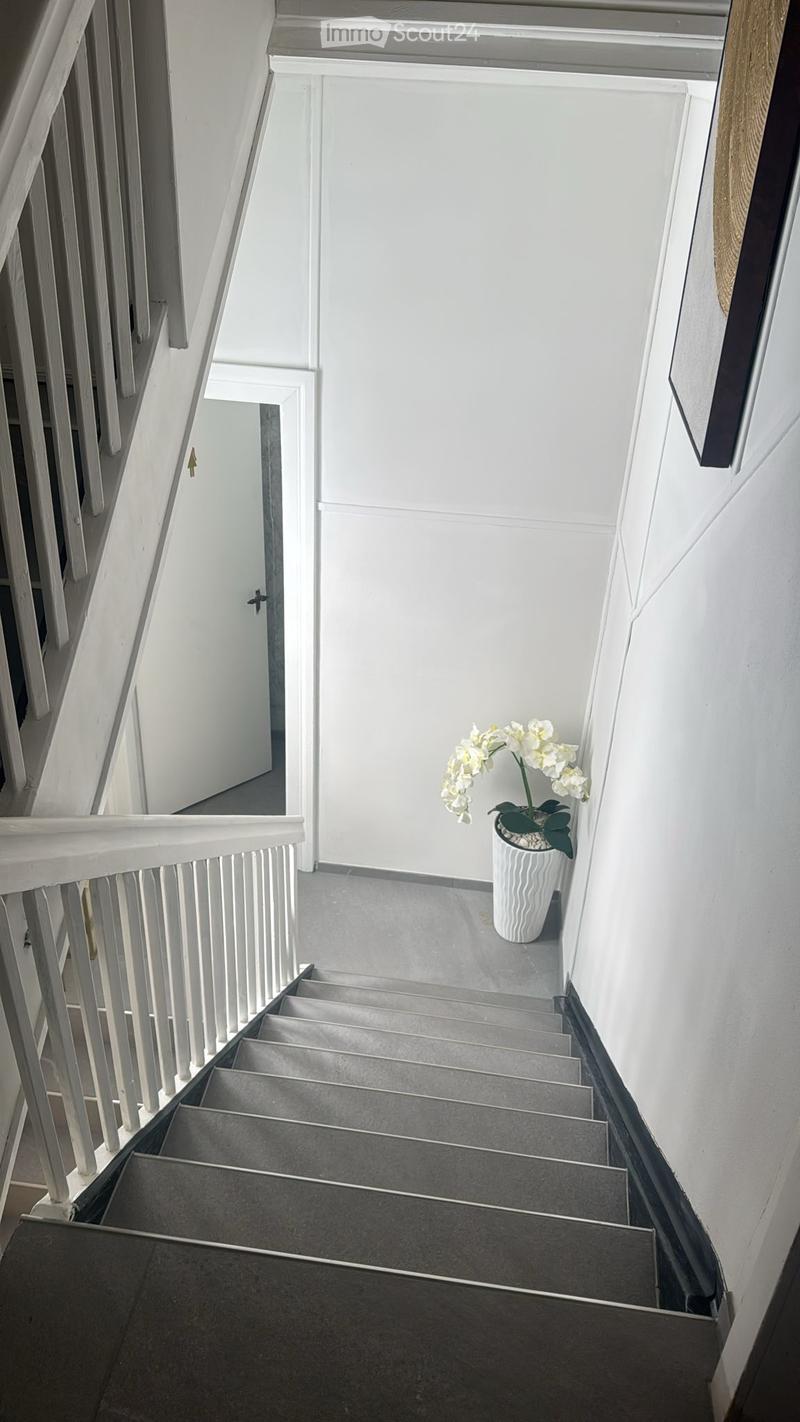 Modern staircase with grey steps, white railing, and a single white flower pot on the landing.