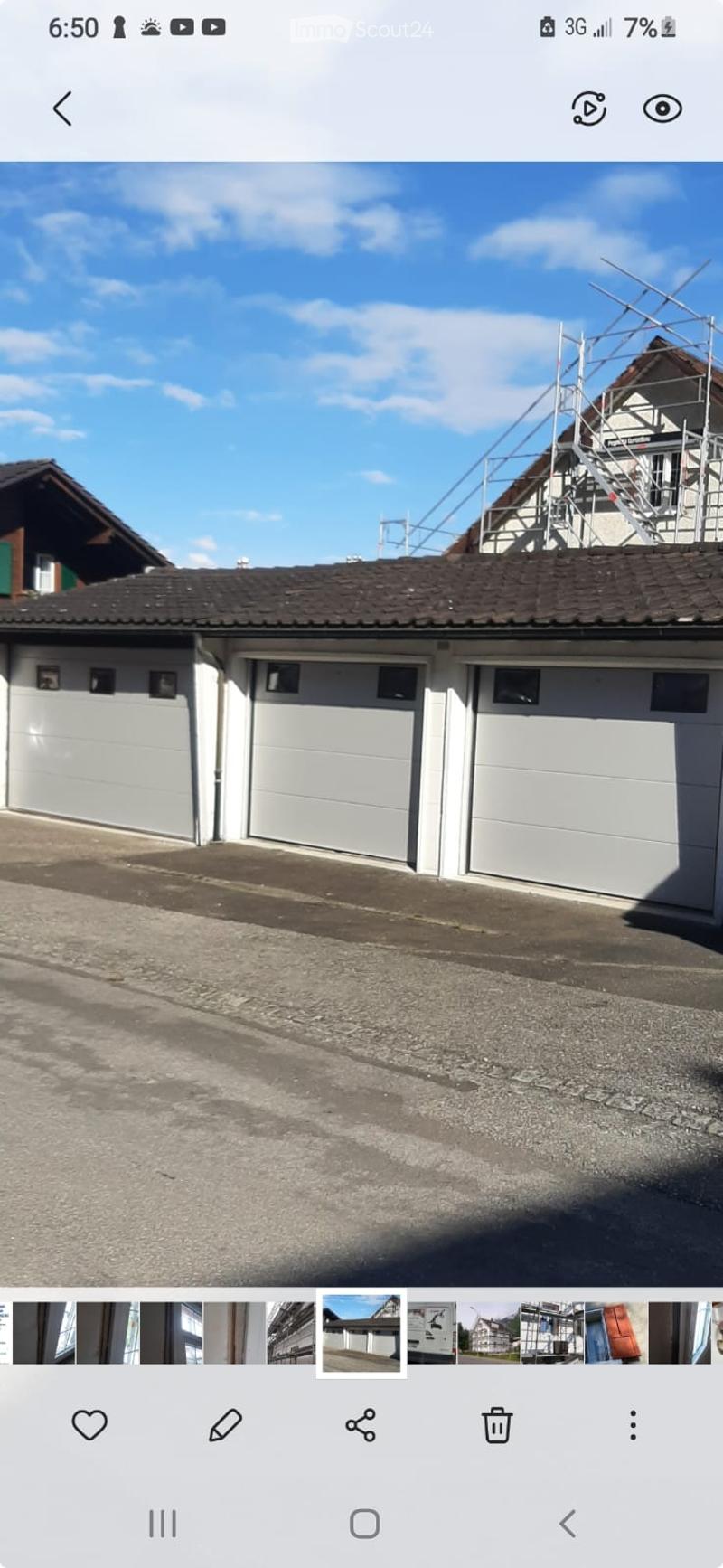 A row of three white garage doors on a building with a dark tiled roof, under a clear blue sky.