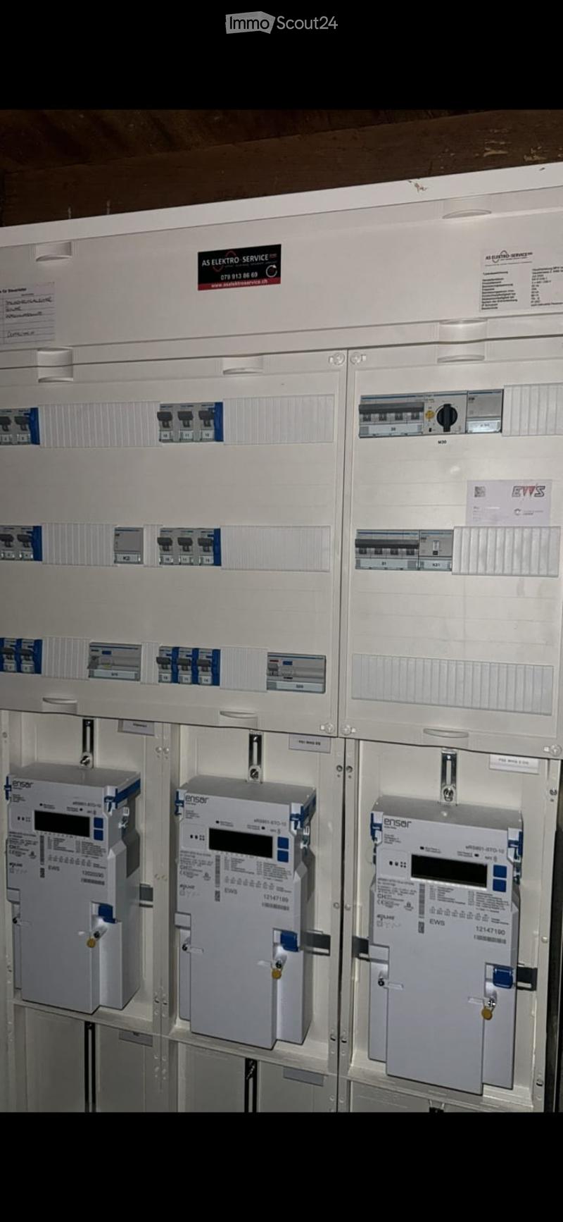 Electrical panel with multiple circuit breakers, switches, and meters mounted on a white panel.