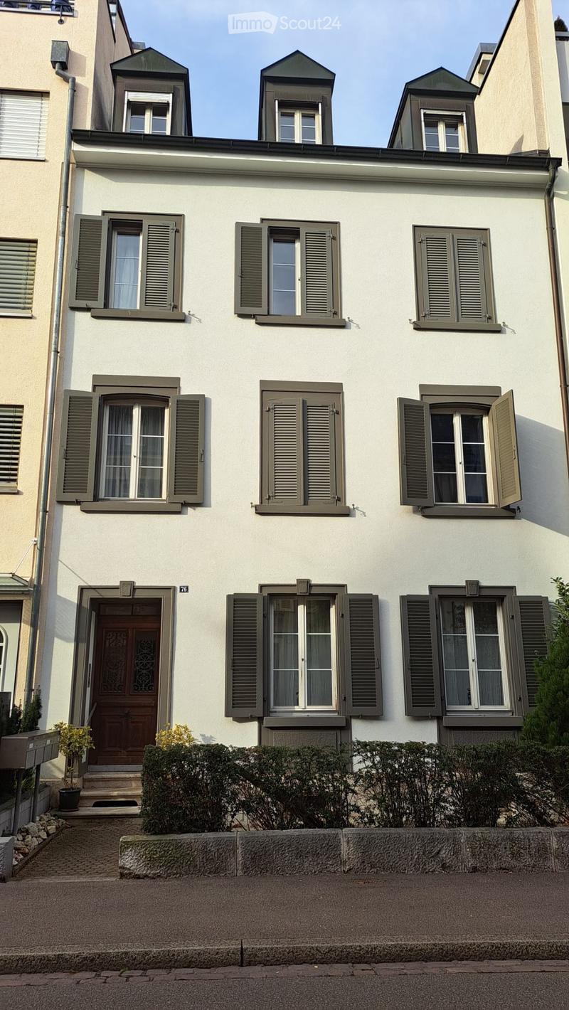 A three-story residential house with white walls, multiple windows with green shutters, and a central wooden front door.