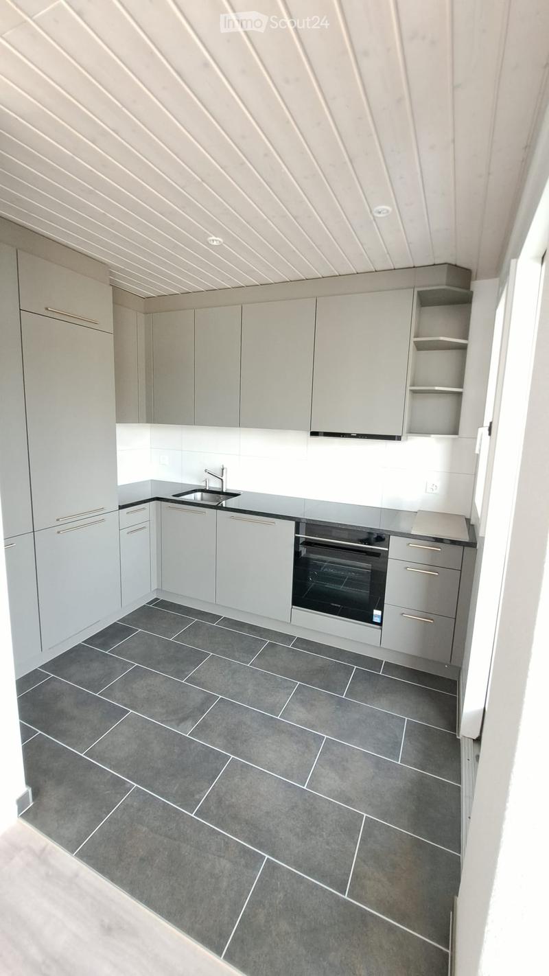 Modern kitchen with grey cabinets, a sink, and an oven, featuring grey tiled flooring and a sleek design.