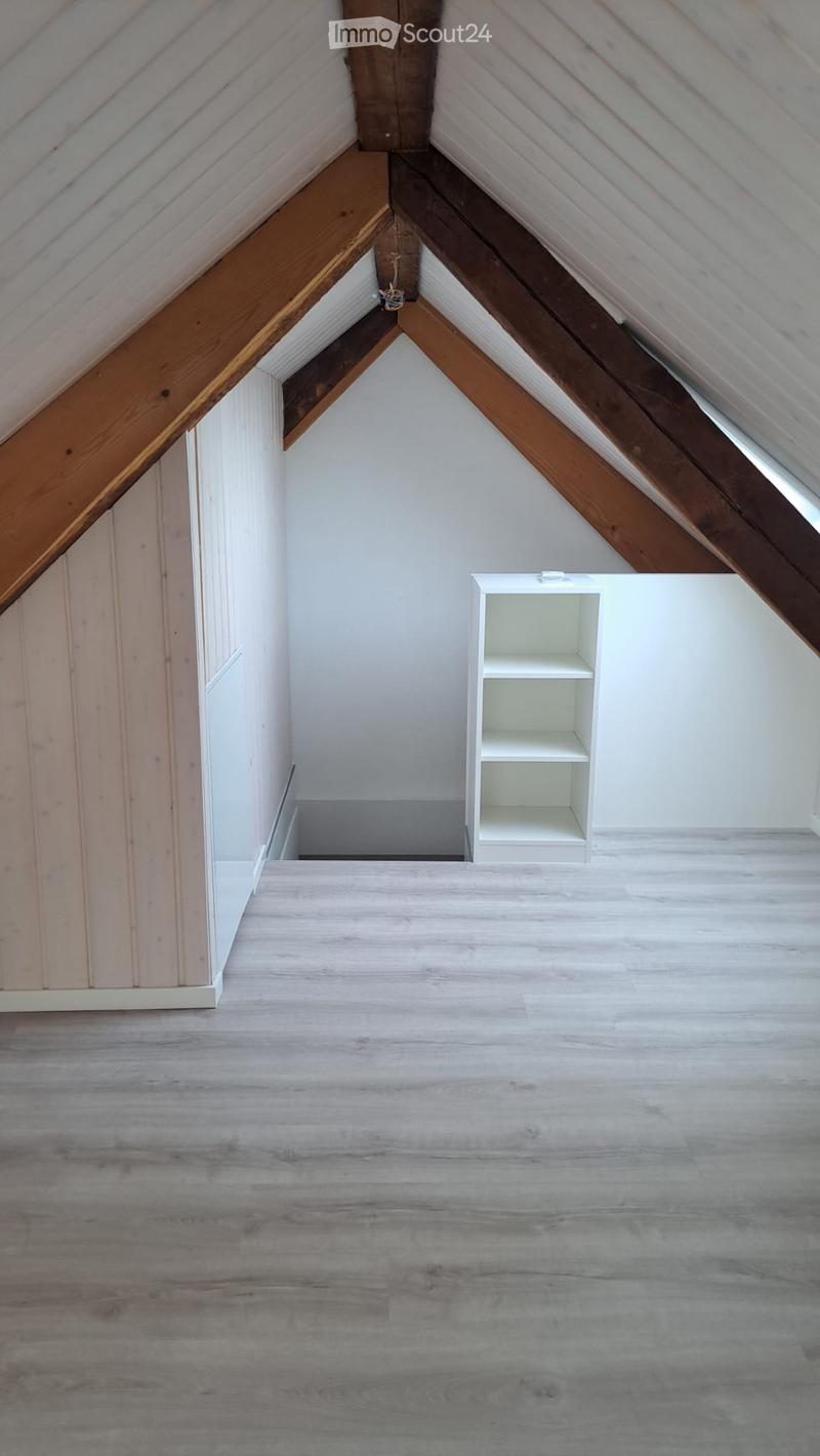 Empty attic space with wooden beams, white walls, and a small white shelf unit.