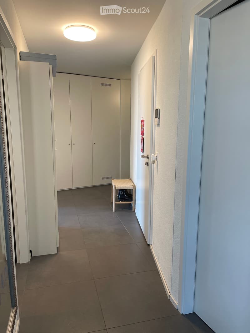 Clean, modern hallway with tiled floor, white walls, built-in storage cabinets, and a small bench holding shoes.