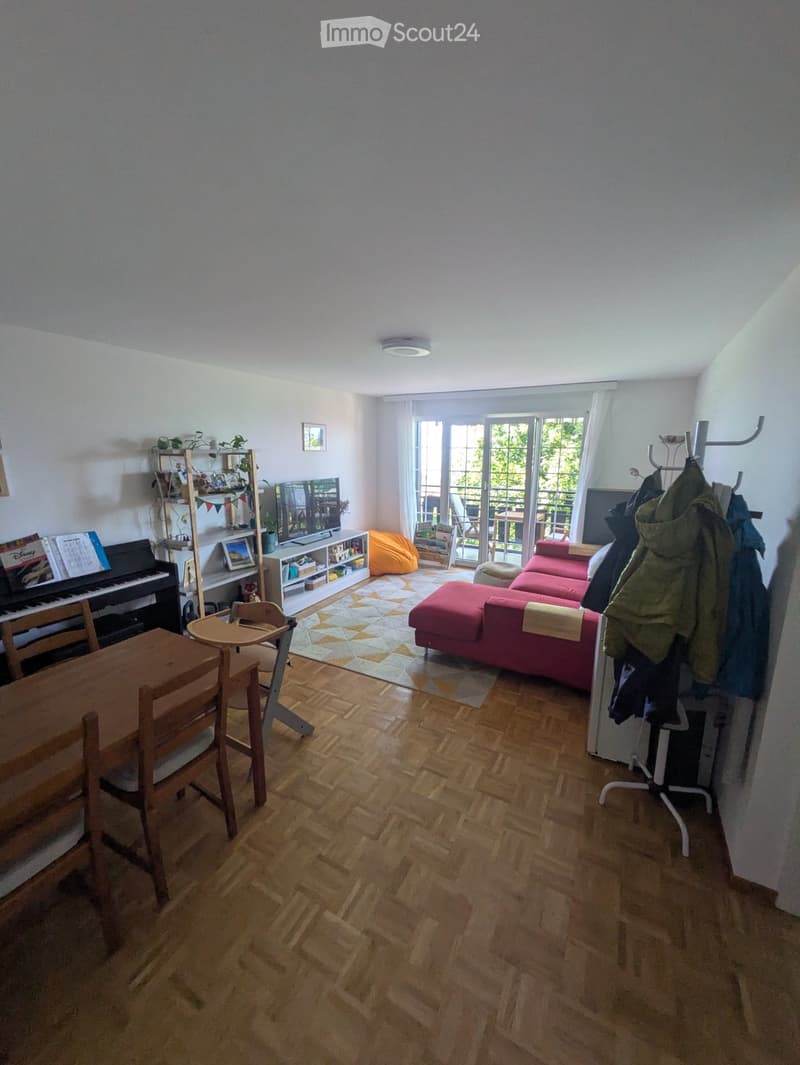 Living room with wooden flooring, a red sofa, a piano, a dining table, and a coat rack near the entrance.