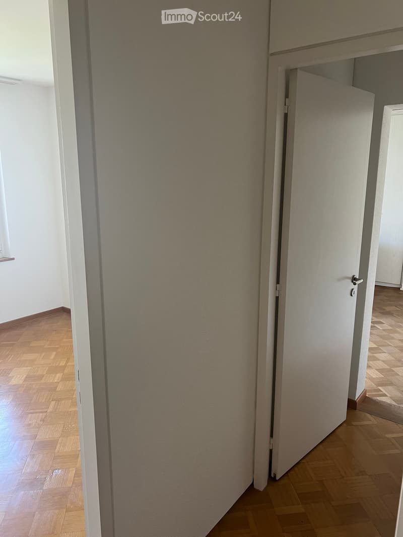 Empty hallway with wooden flooring, white walls, and a partially open door leading to another room.