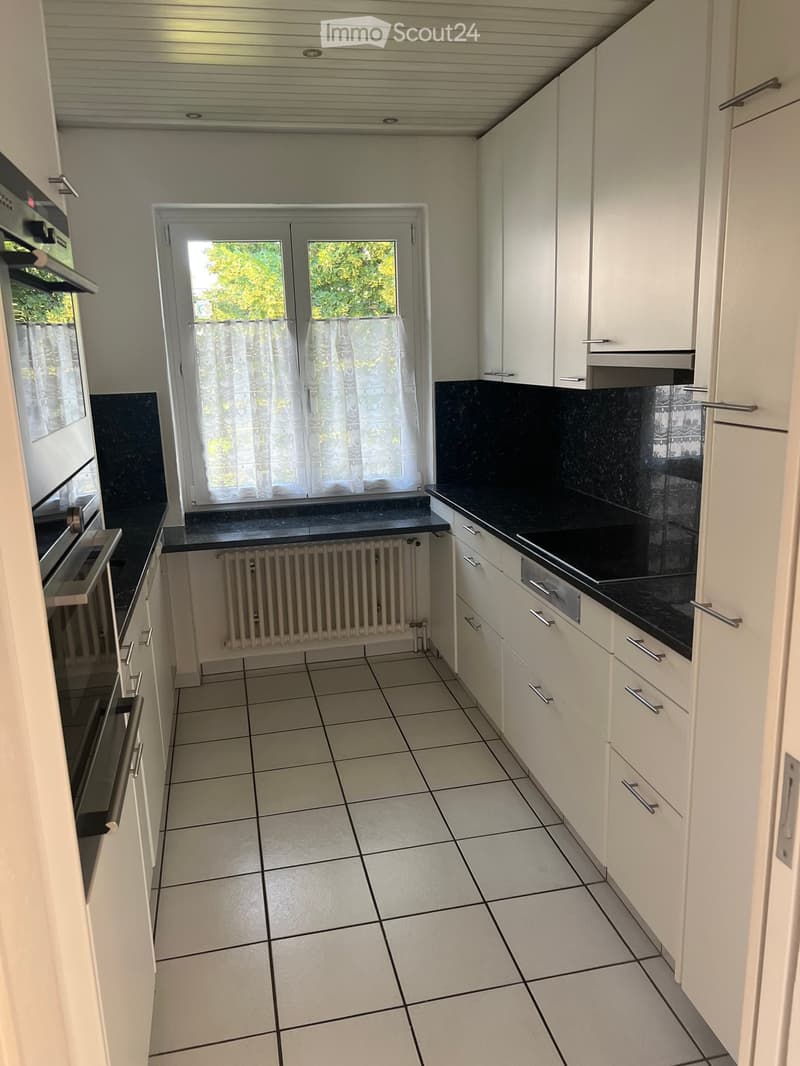 Modern kitchen with white cabinets, black countertops, tiled floor, and a window with sheer curtains.
