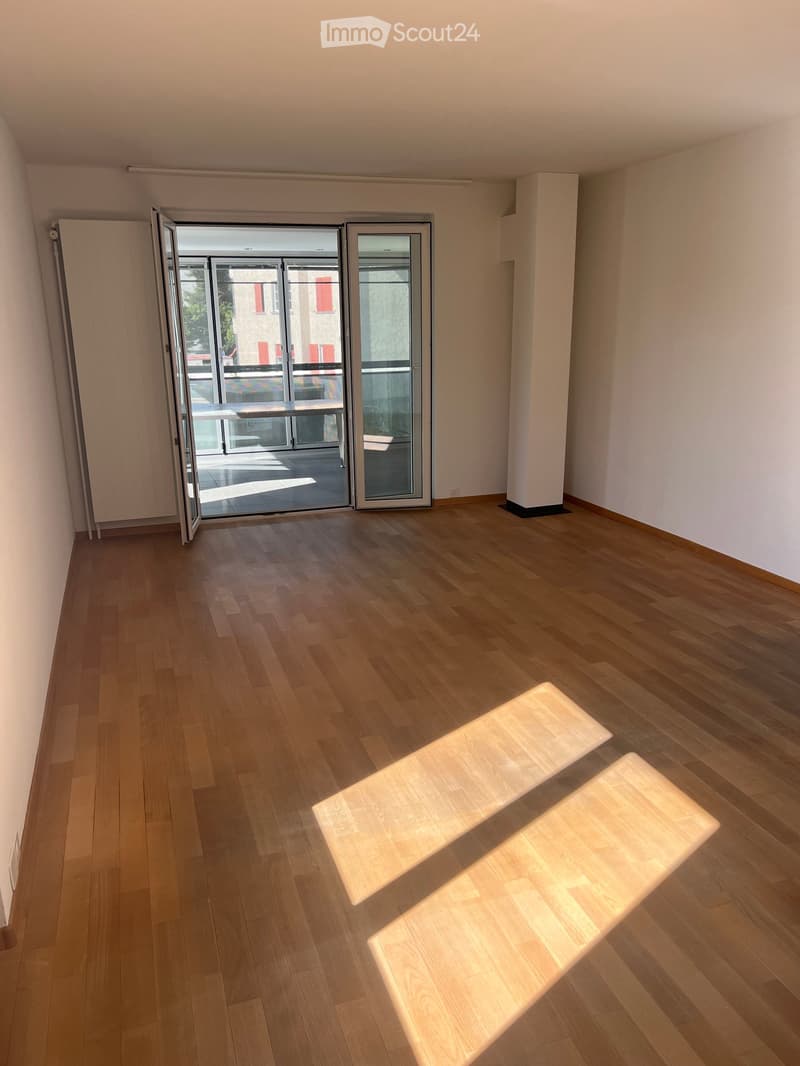 Empty room with wooden flooring, white walls, and large sliding glass doors leading to a balcony.