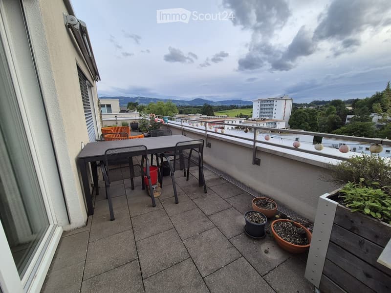 Balcony with tiled floor, metal railing, and outdoor furniture including a table, chairs, and potted plants.