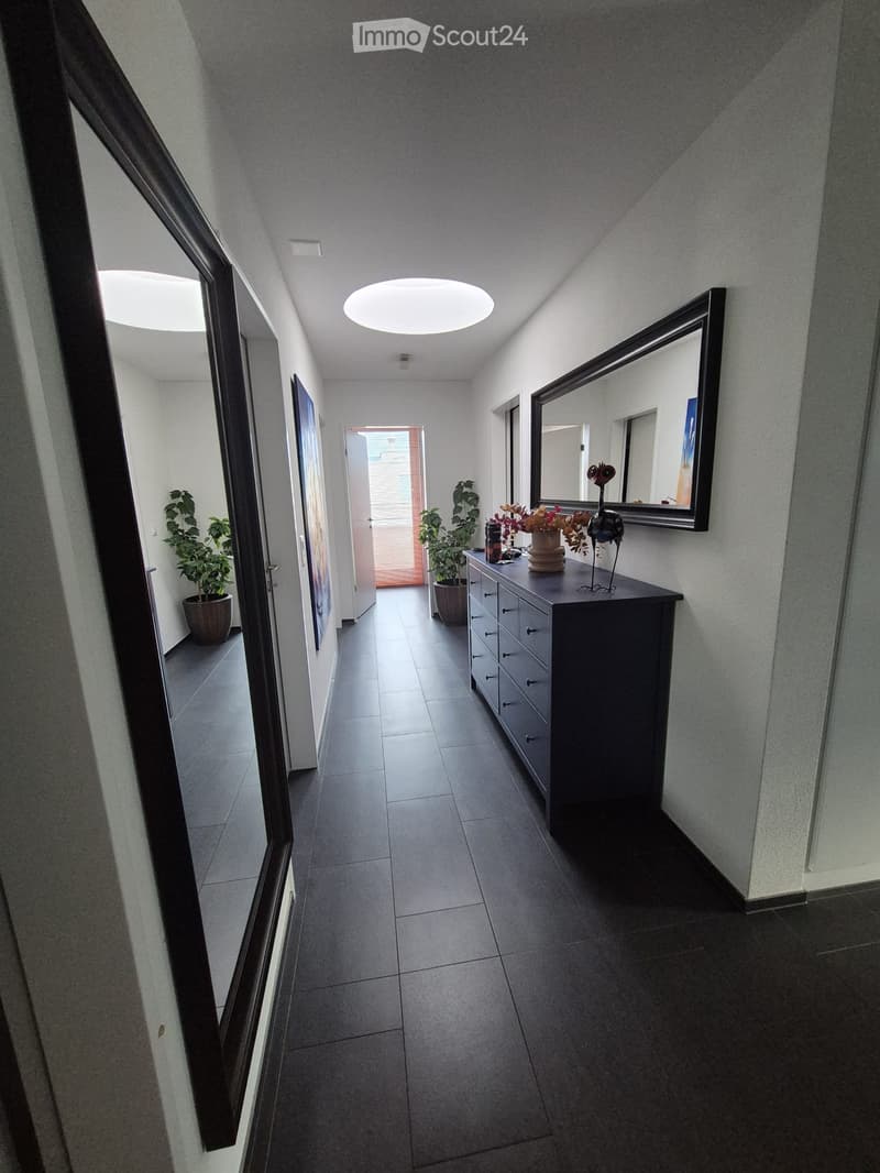 Modern hallway with tiled floor, grey walls, round ceiling light, and a small table with a vase and decorative items.