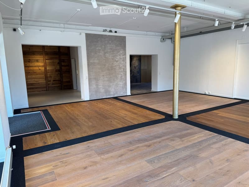 Empty room with wooden flooring, white walls, exposed ceiling beams, and a large wooden door in the background.
