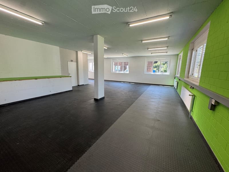 Empty room with green and white walls, dark flooring, and large windows. No furniture or equipment present.