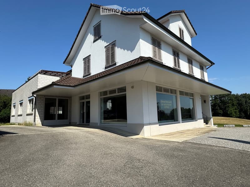 Two-story white building with a brown tiled roof, multiple windows, and a covered entrance area with glass doors.