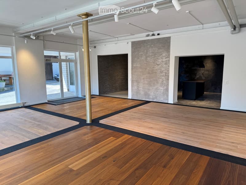 Empty room with polished wooden flooring, white walls, large windows, and a central gold-colored column. No furniture or equipment present.