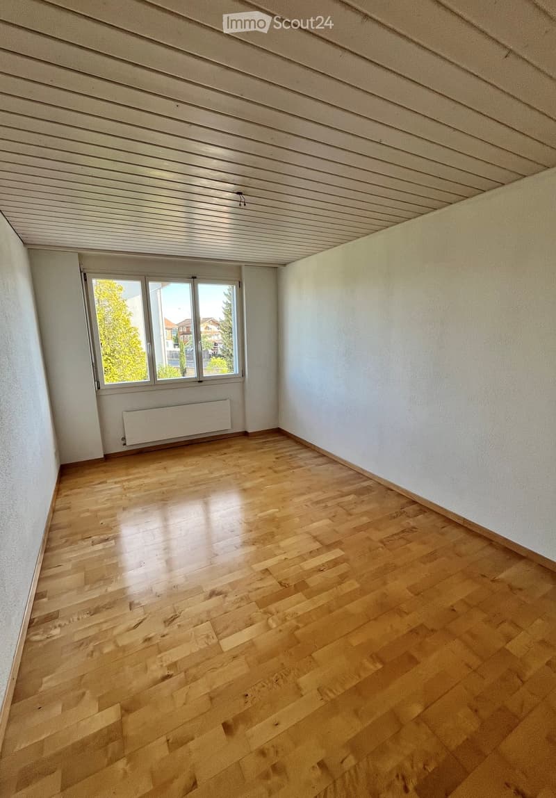 Empty room with wooden flooring, white walls, and a large window with a radiator below it.