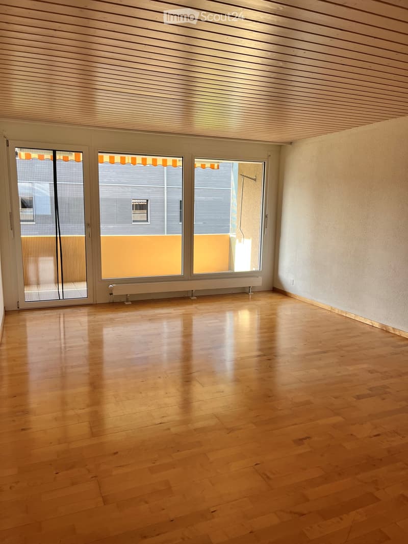 Empty room with wooden flooring, large windows with blinds, and white walls.