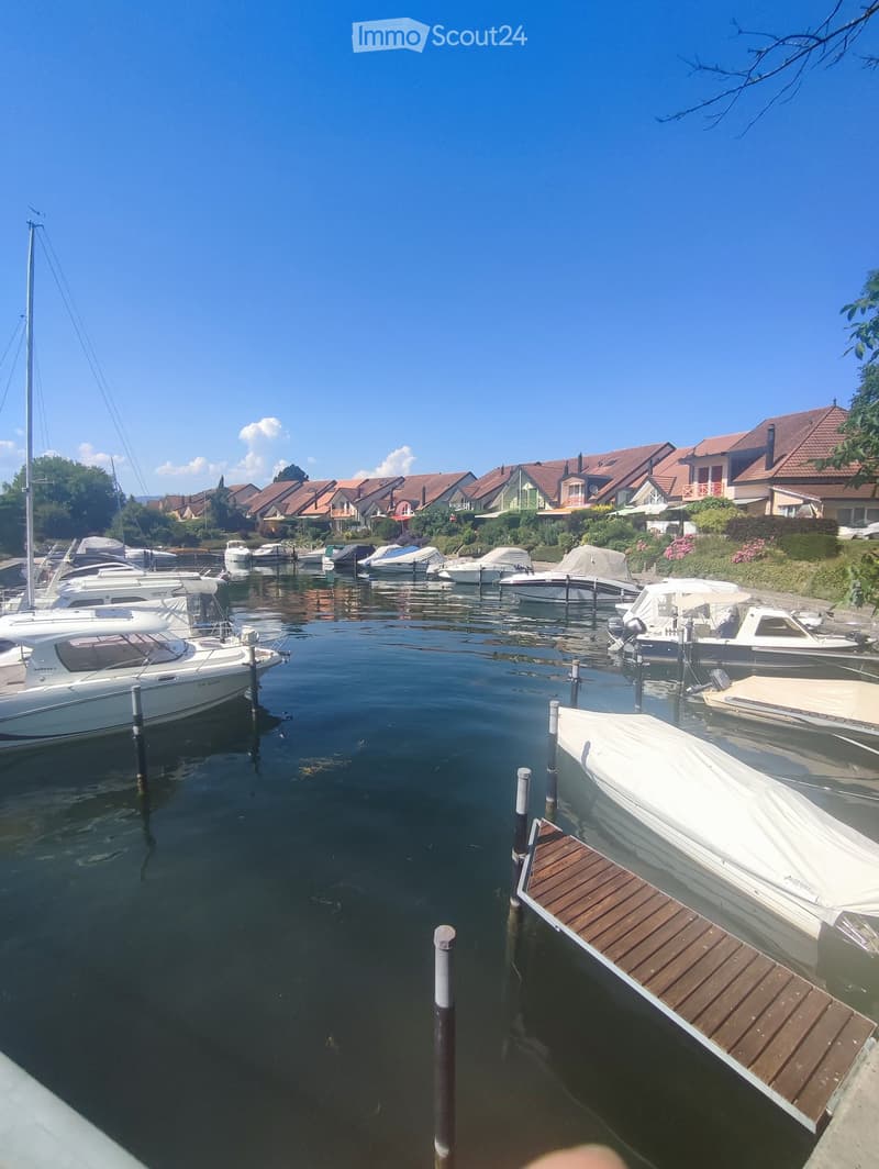 A serene marina with several docked boats, surrounded by residential houses with red-tiled roofs and lush greenery.