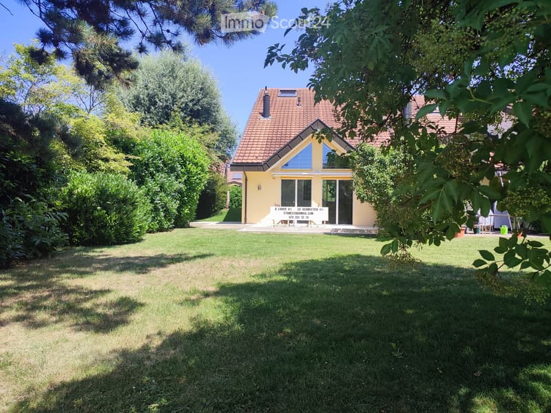 A well-maintained garden with a lawn, surrounded by trees and a yellow house with a red-tiled roof in the background.