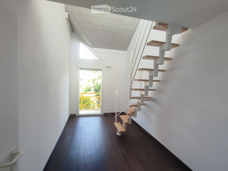 Modern hallway with dark wooden flooring, white walls, and a spiral staircase leading upwards. Features a glass door with a yellow frame leading outside.