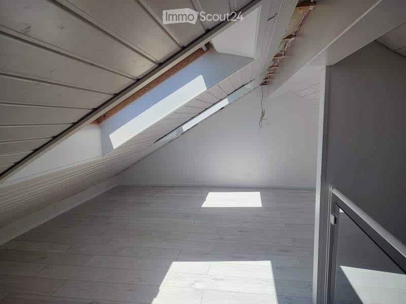 Empty attic space with wooden flooring, white walls, exposed wooden beams, and skylight windows allowing natural light.