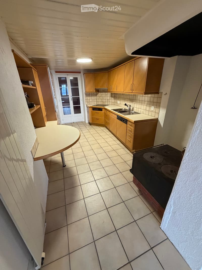 Kitchen with light wooden cabinets, tiled floor, sink, stove, and a round table.