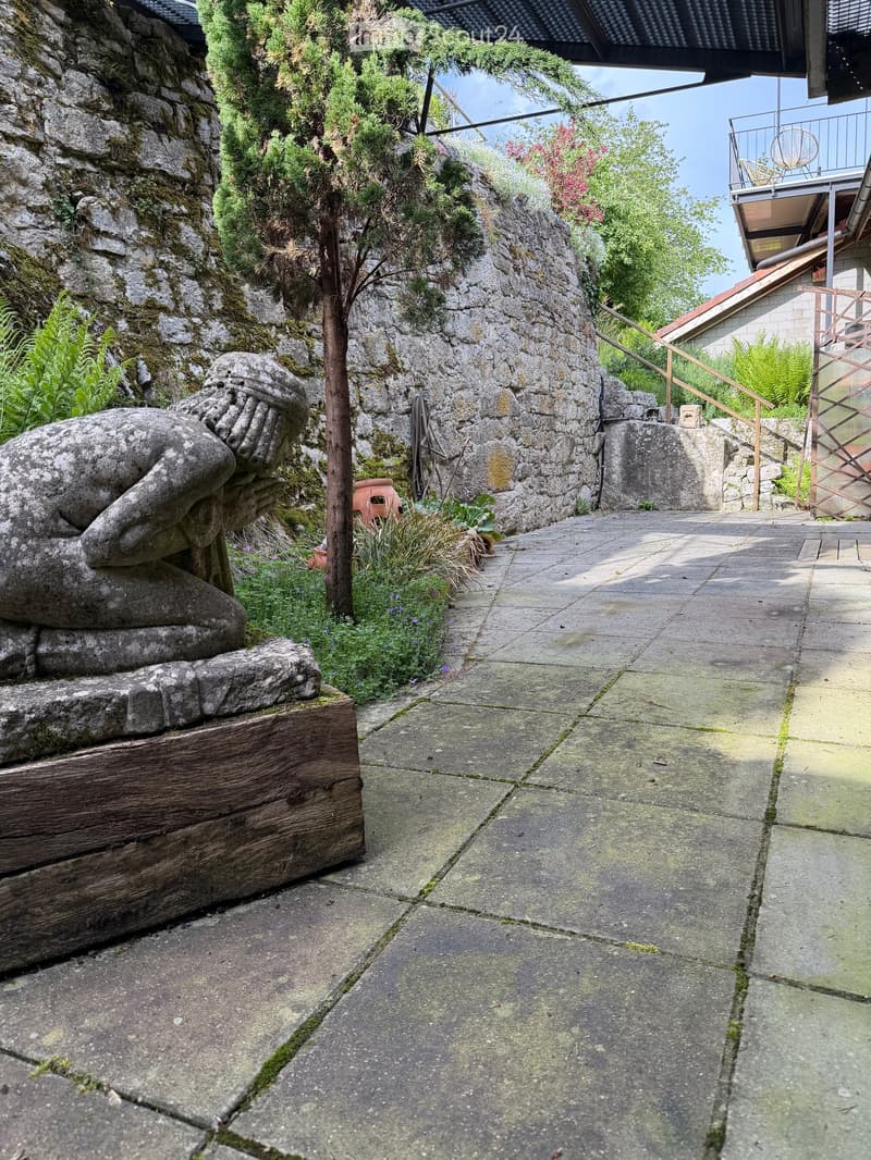 Garden pathway with stone statue, wooden steps, and greenery.