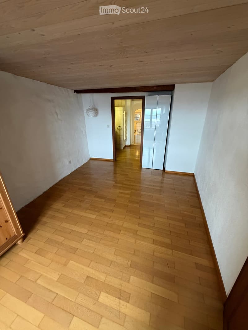 Empty hallway with wooden flooring, white walls, and a visible doorway leading to another room.