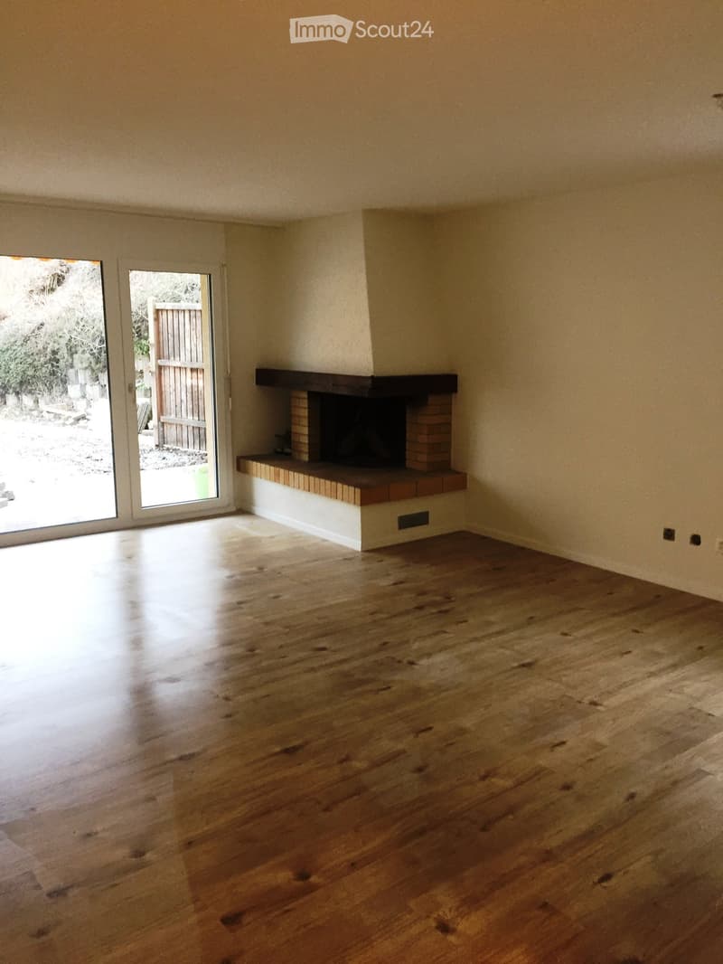 Empty room with wooden flooring, fireplace, and large sliding glass doors leading to an outdoor area.