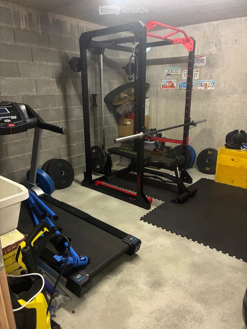 A well-equipped home gym with a treadmill, weight machine, weight plates, and storage boxes.