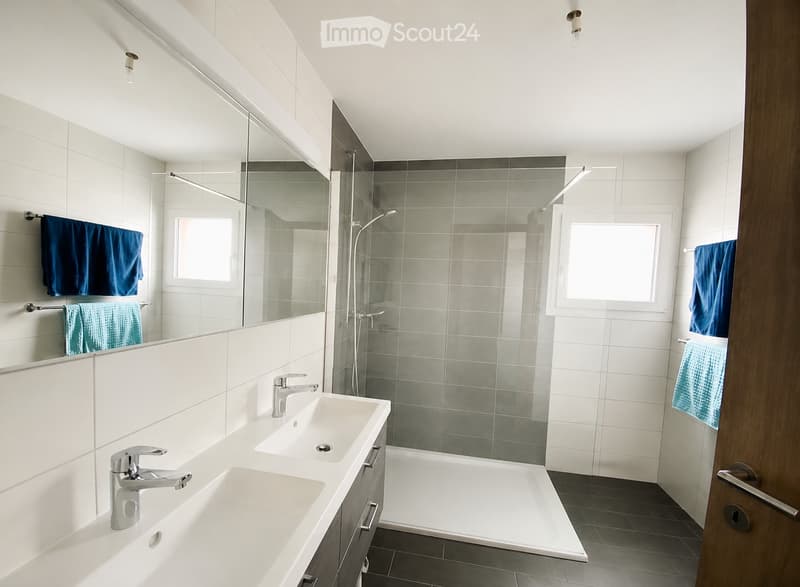 Modern bathroom with two sinks, a bathtub, a large mirror, and blue towels hanging on the walls.
