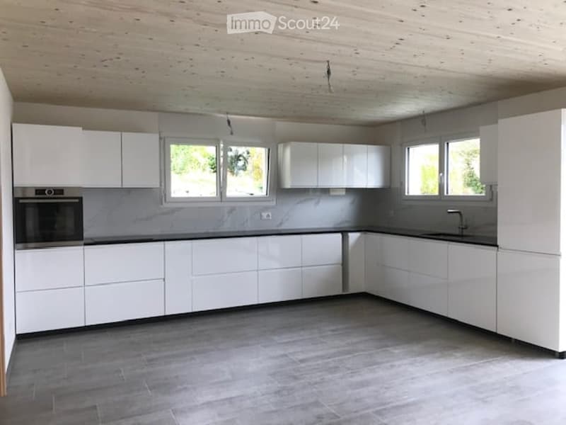 Modern, minimalist kitchen with white cabinets, a central island, and grey countertops. Features include an integrated oven and a sink with a modern faucet.