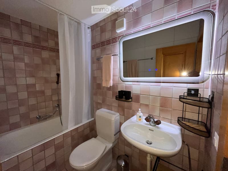 Bathroom with beige tiles, a toilet, a sink with a modern mirror, a shower area with a curtain, and a towel hanging on the wall.