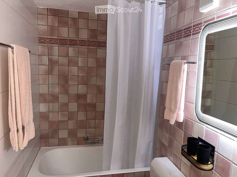 Bathroom with a bathtub, tiled walls, a shower curtain, a mirror, and towels on the rack.