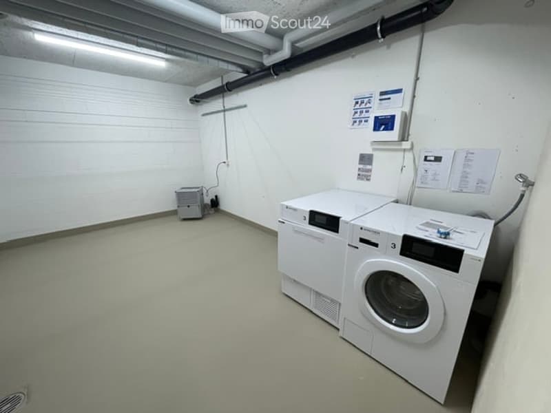 Clean, well-lit laundry room with white washing machine and dryer, control panels, and a small electrical unit in the corner.