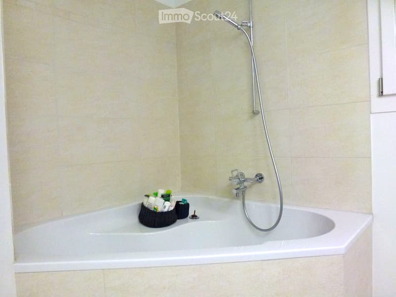 Bathtub with a handheld shower hose and a small basket holding toiletries on the edge.