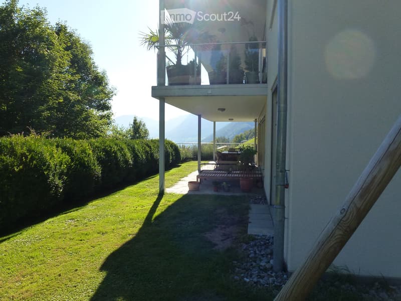 Garden area with a well-maintained lawn, wooden deck, potted plants, and a covered balcony area with outdoor furniture.