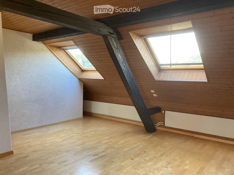 Empty attic room with wooden floors, exposed wooden beams, and skylight windows allowing natural light.