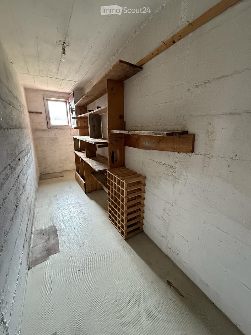 Empty room with unfinished concrete walls, wooden shelves, and a stack of wooden crates on the floor.