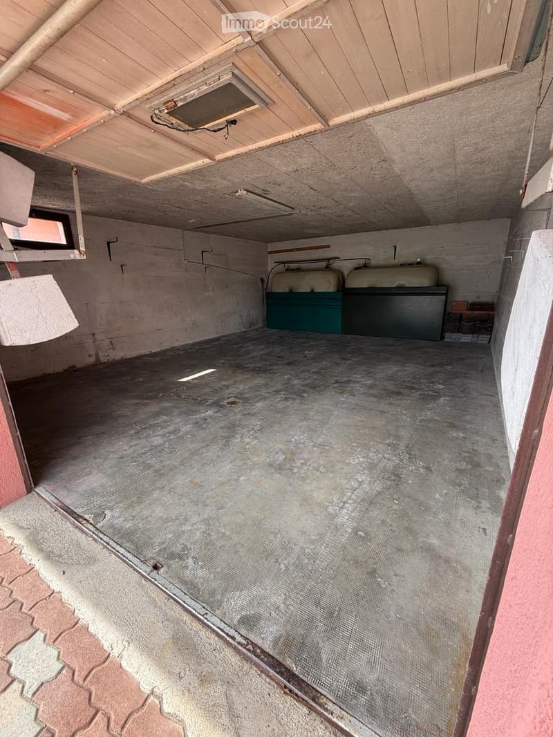 Empty garage with concrete floor, exposed wooden ceiling, and two large storage containers in the back.