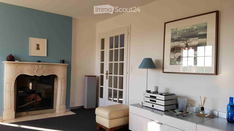 Living room with a stone fireplace, cream ottoman, modern audio system on a white cabinet, and decorative items including vases and framed artwork.