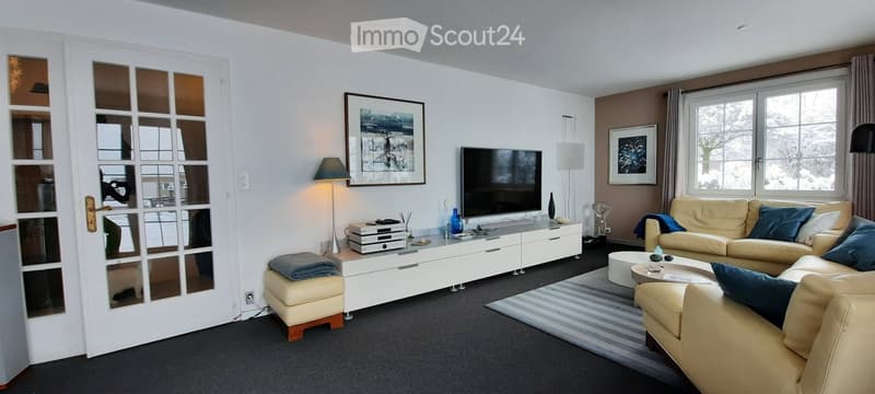 Modern living room with a cream sofa, coffee table, ottoman, TV stand, floor lamp, and picture frames on the wall.