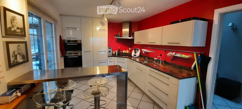 Modern kitchen with white cabinets, stainless steel appliances, red backsplash, and a central island with bar stools.