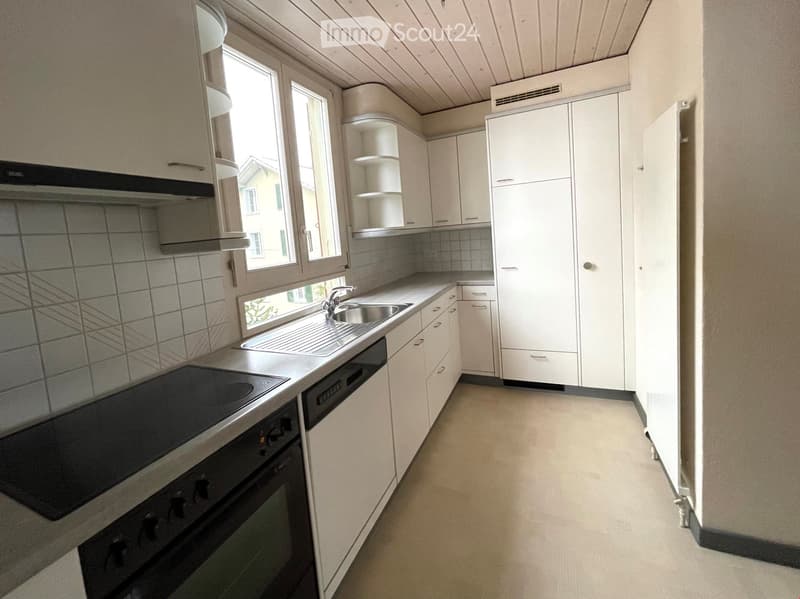 Modern kitchen with white cabinets, stainless steel sink, oven, dishwasher, and built-in storage. Natural light from large windows.