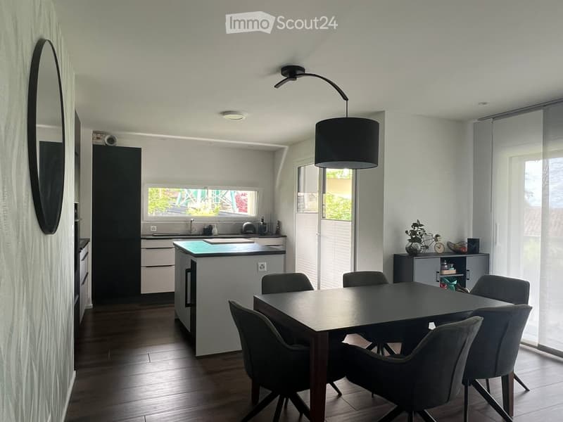 Modern kitchen and dining area with a dark wooden dining table, six chairs, a kitchen island, and various appliances.